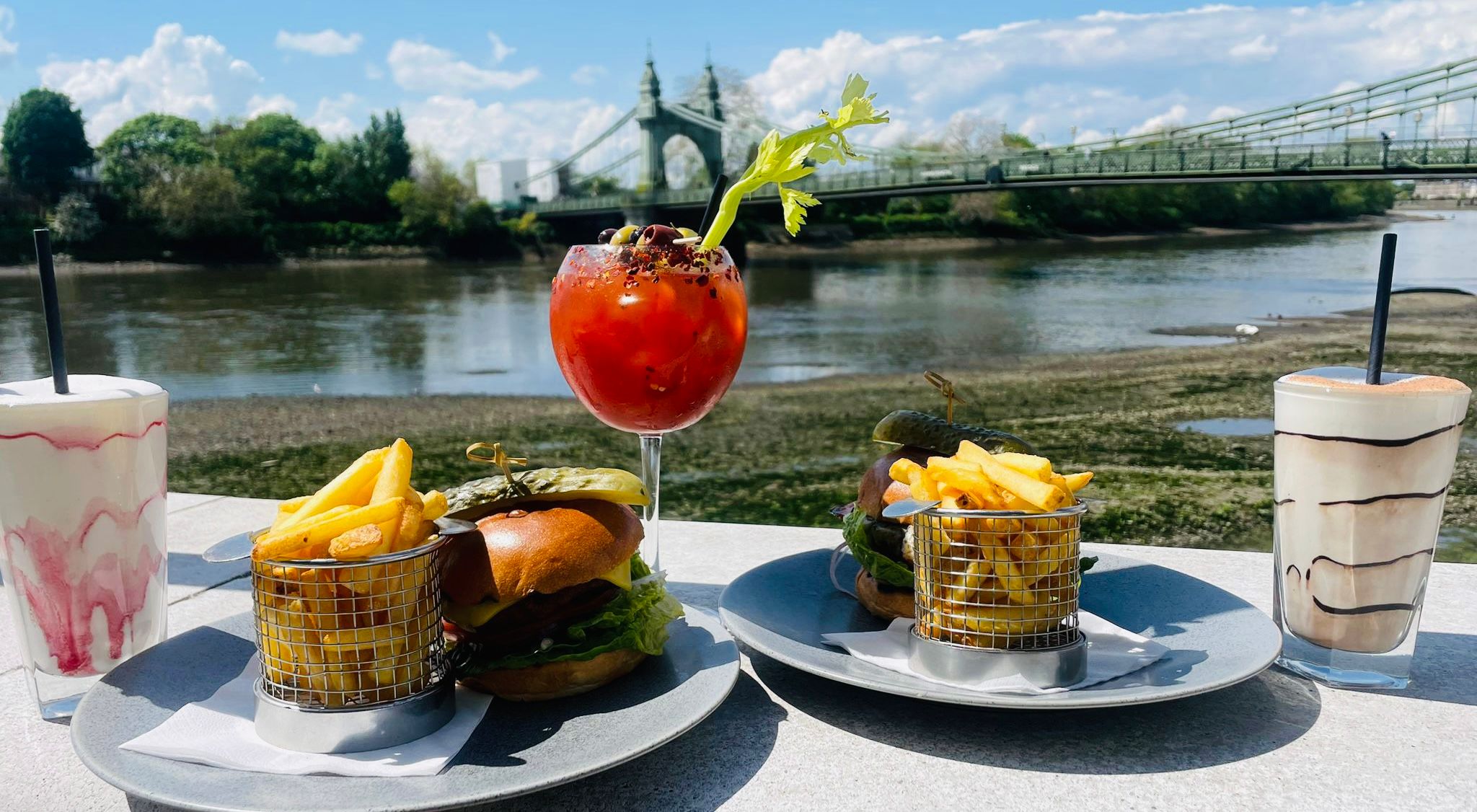 Table filled with cocktails, milkshake, and two burgers